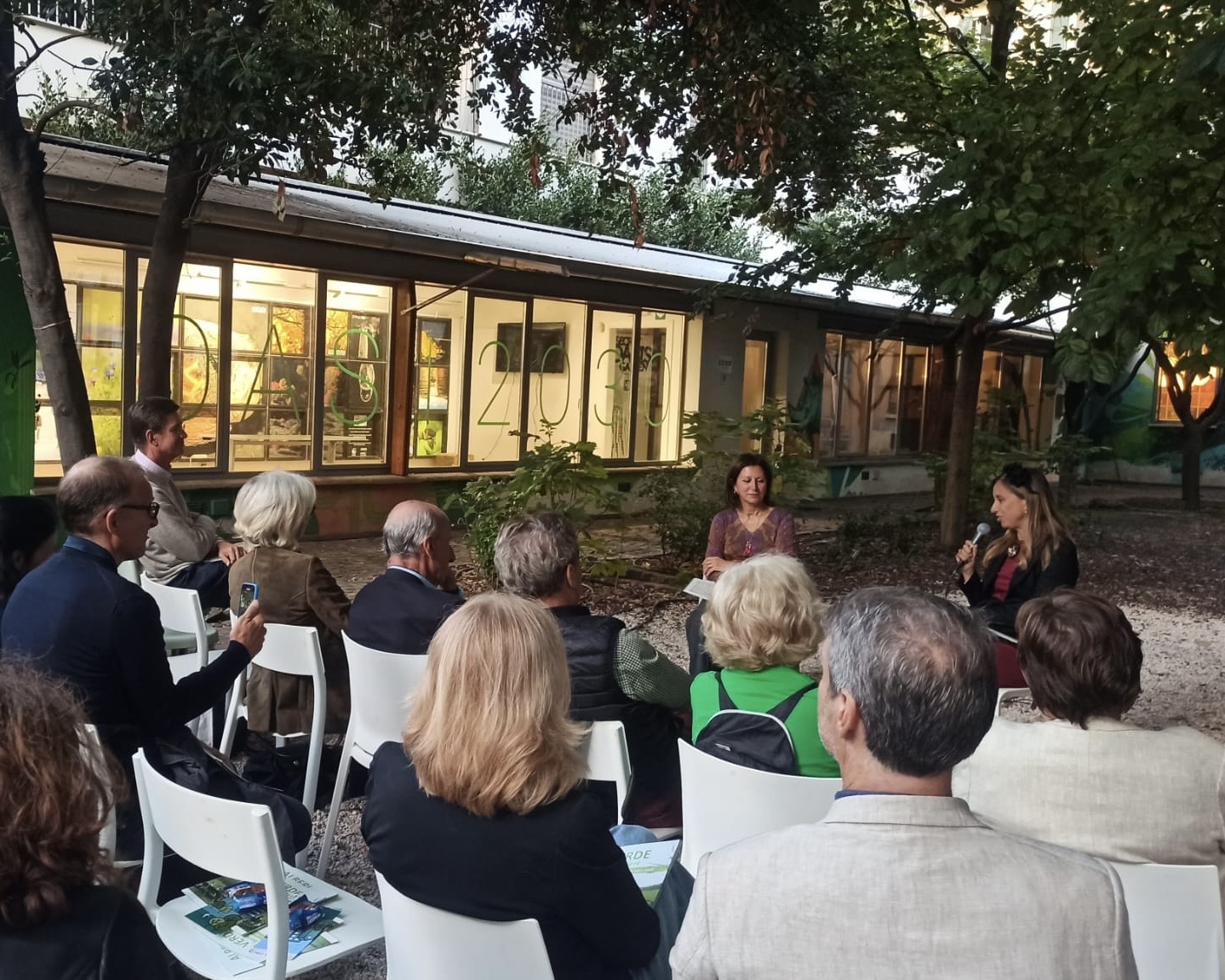 People on chairs in a garden, evening, listening to two female speakers
