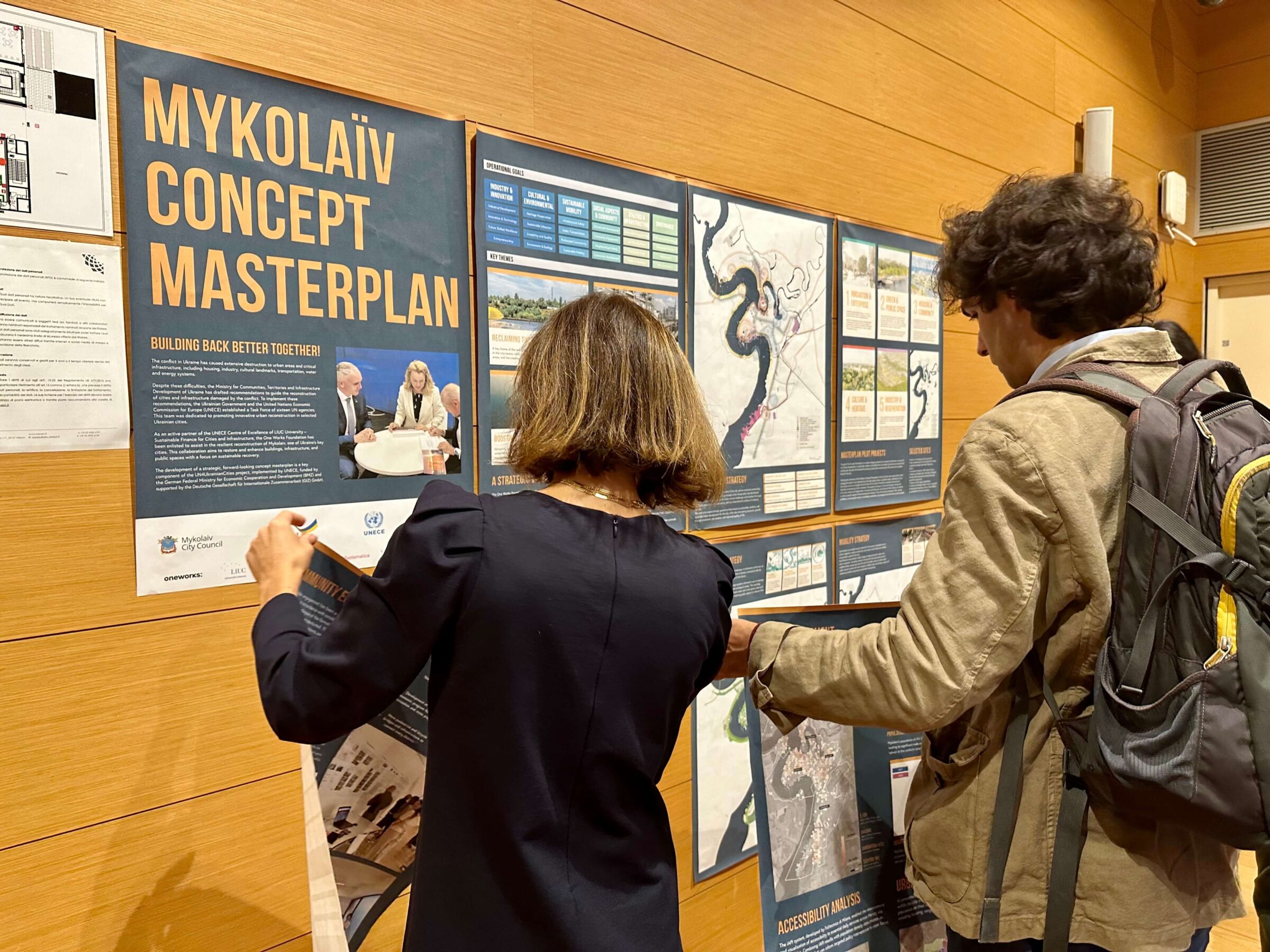 A woman and a man in front of a poster regarding the reconstruction of Mykolayev in Ukraina