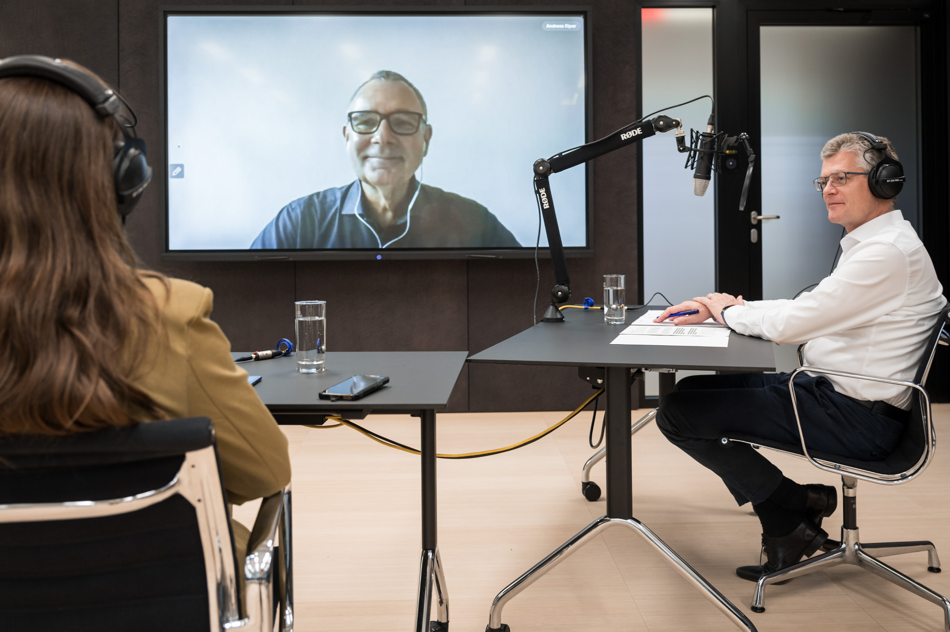 two people sitting at desks and a man connected via screen
